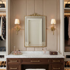 Two Clérachic brass sconces with pleated shades flank an arch-topped mirror above a marble-topped dressing table in a dressing room.