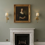 Clérachic wall lights with beige pleated shades hang either side of a gilt-framed portrait, above a white marble fireplace on a sage wall.