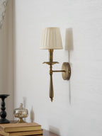 Side view of a Clérachic wall sconce showing its brass arm, round backplate and pleated shade, above a stack of books.