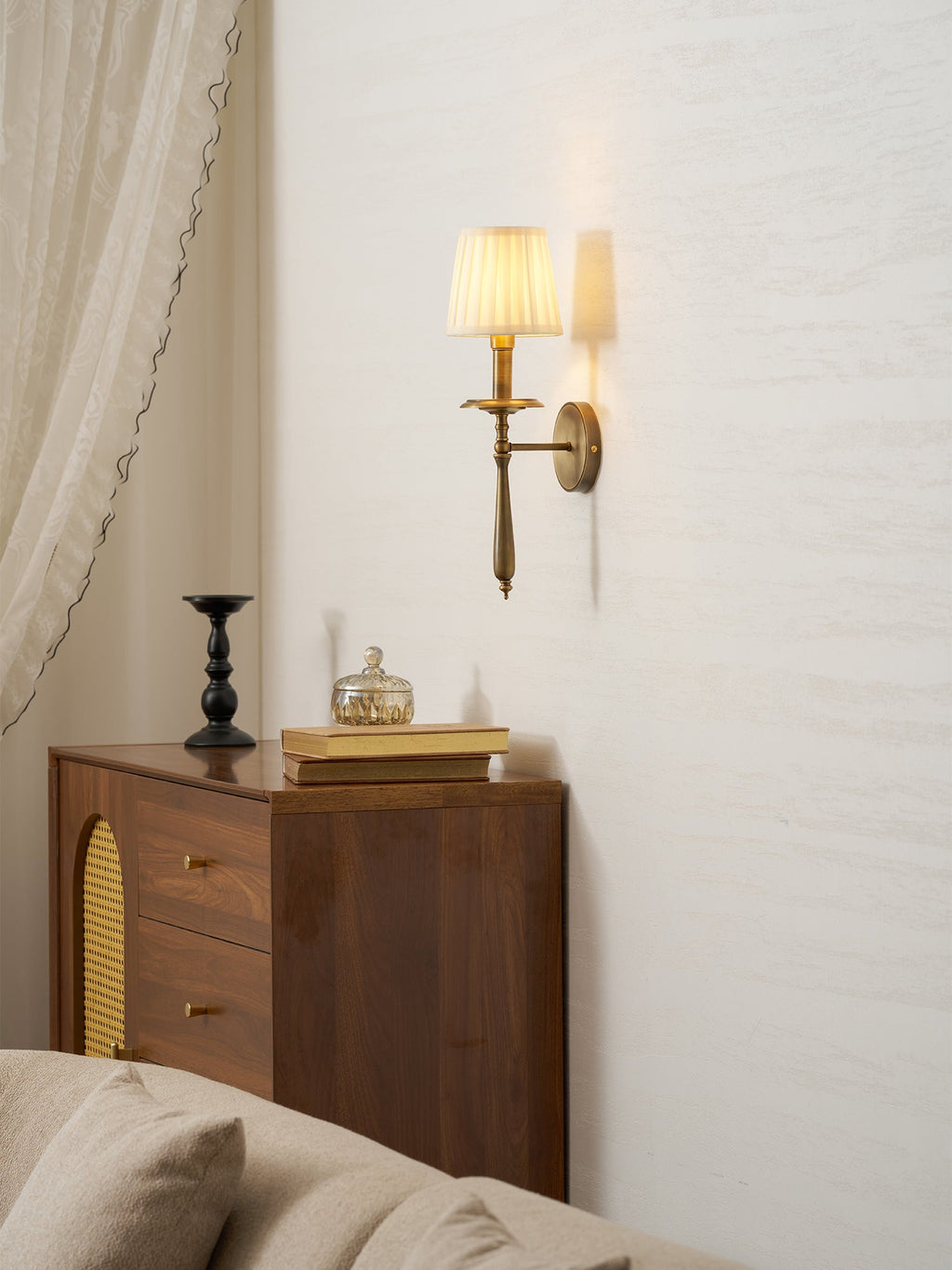 Clérachic brass wall sconce high on a pale wall above a walnut cabinet with cane-panel doors and a cream sofa.