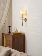 Clérachic brass wall sconce high on a pale wall above a walnut cabinet with cane-panel doors and a cream sofa.