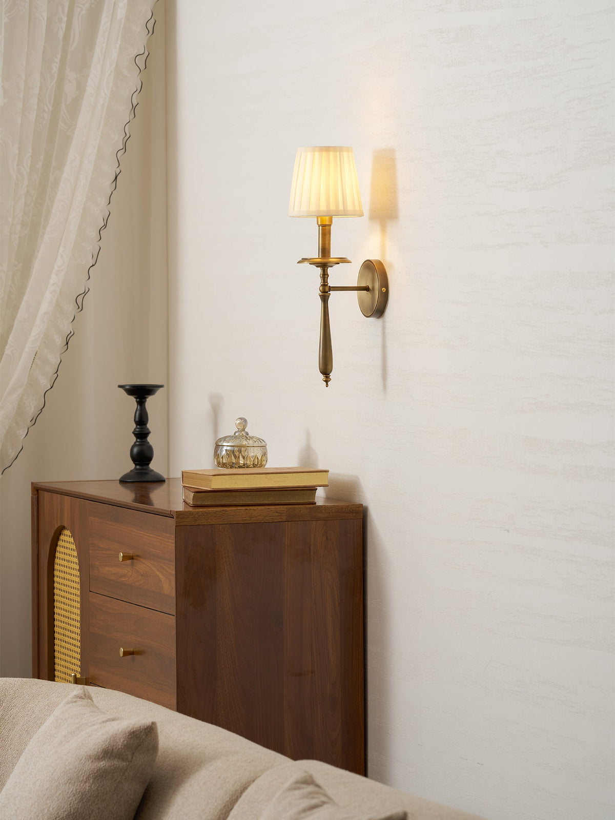 Clérachic brass wall sconce high on a pale wall above a walnut cabinet with cane-panel doors and a cream sofa.