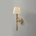 Antique brass Clérachic wall light with a pleated beige shade, shown unlit against a mid-grey wall.