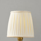 Close view of the beige pleated fabric shade of this Clérachic wall light, with a trimmed top and bottom edge.
