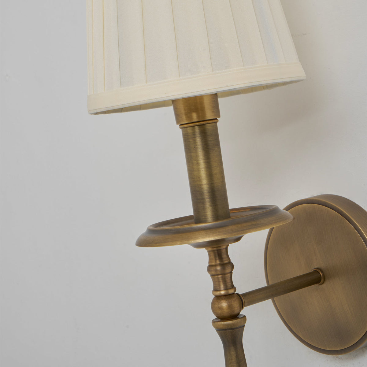 Close view of the brass drip tray, turned stem and round backplate of this Clérachic wall light, under the pleated shade.