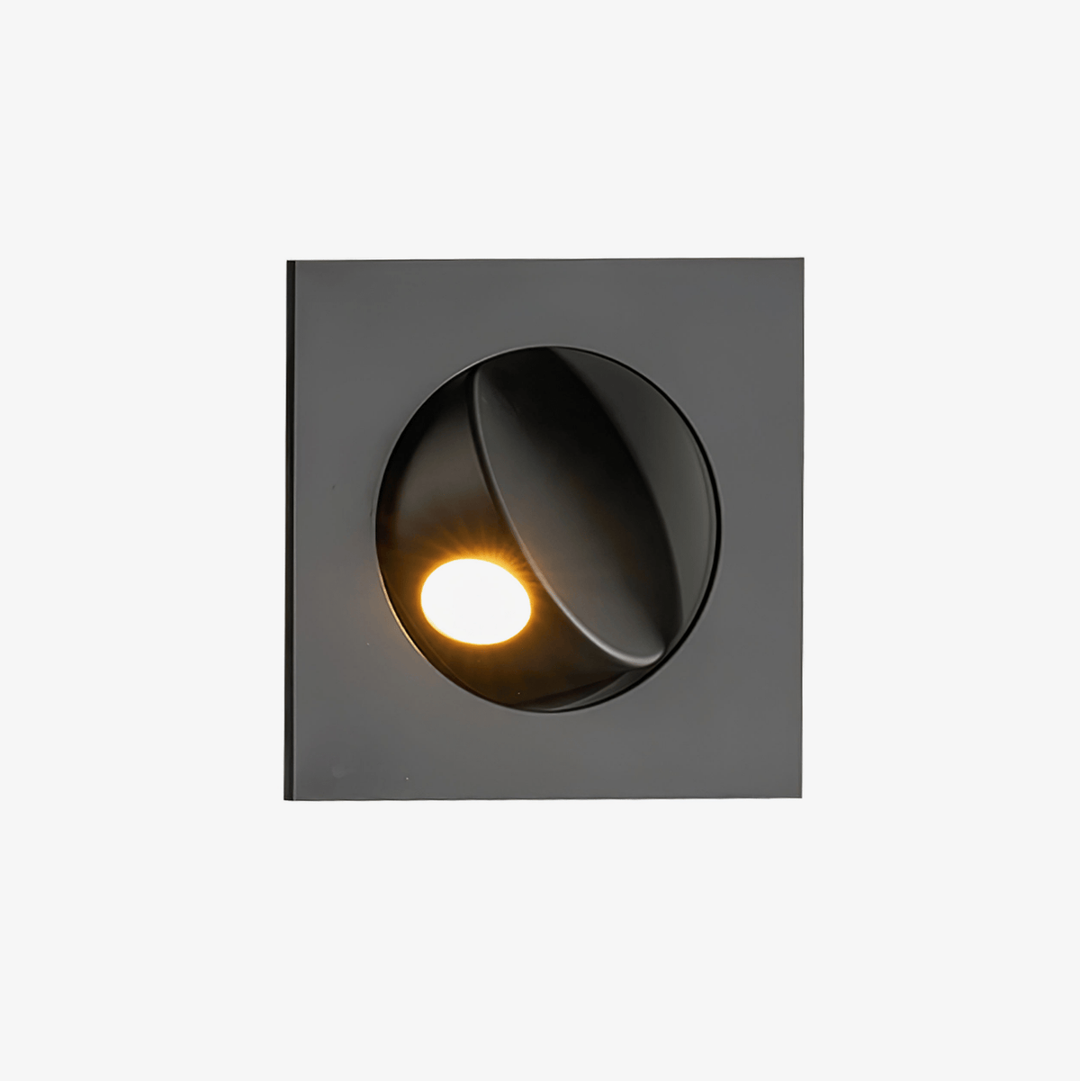 Black square recessed wall light from Clérachic with a round opening and a swivelling hood, lit with a warm LED, on a plain light backdrop.