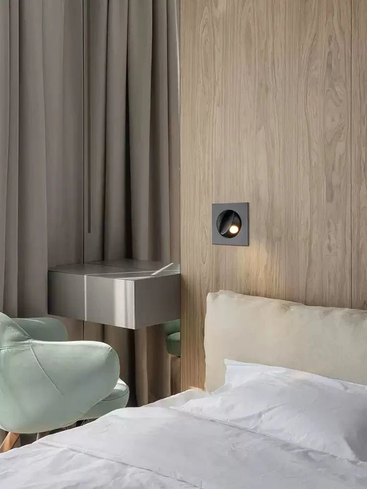 Black Clérachic recessed wall light set in a wooden wall beside grey curtains, a pale green armchair and a narrow grey desk.