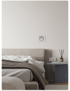 White-finish Clérachic recessed wall light, unlit, on a white wall above a grey bed, a bedside table and a reed diffuser.