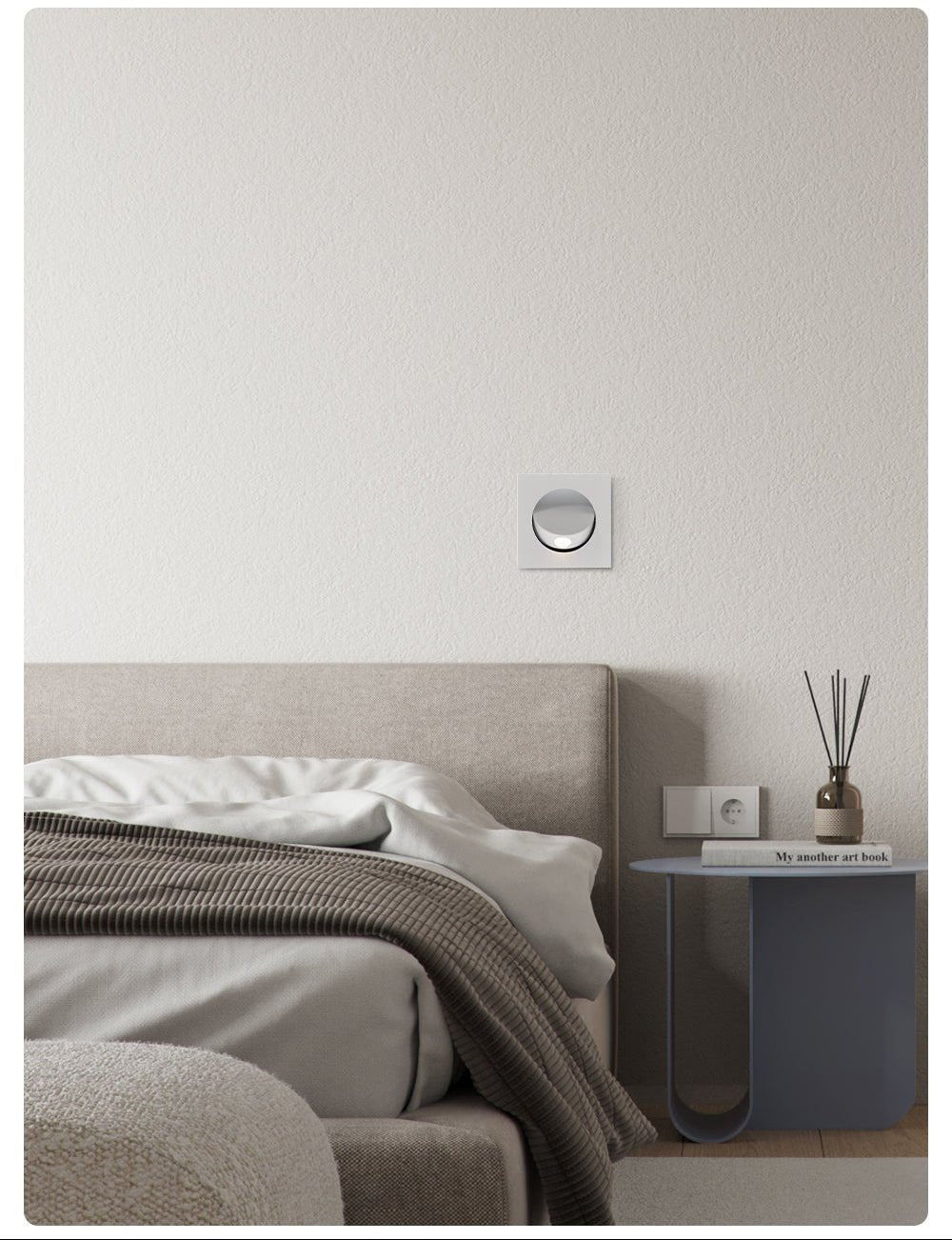 White-finish Clérachic recessed wall light, unlit, on a white wall above a grey bed, a bedside table and a reed diffuser.