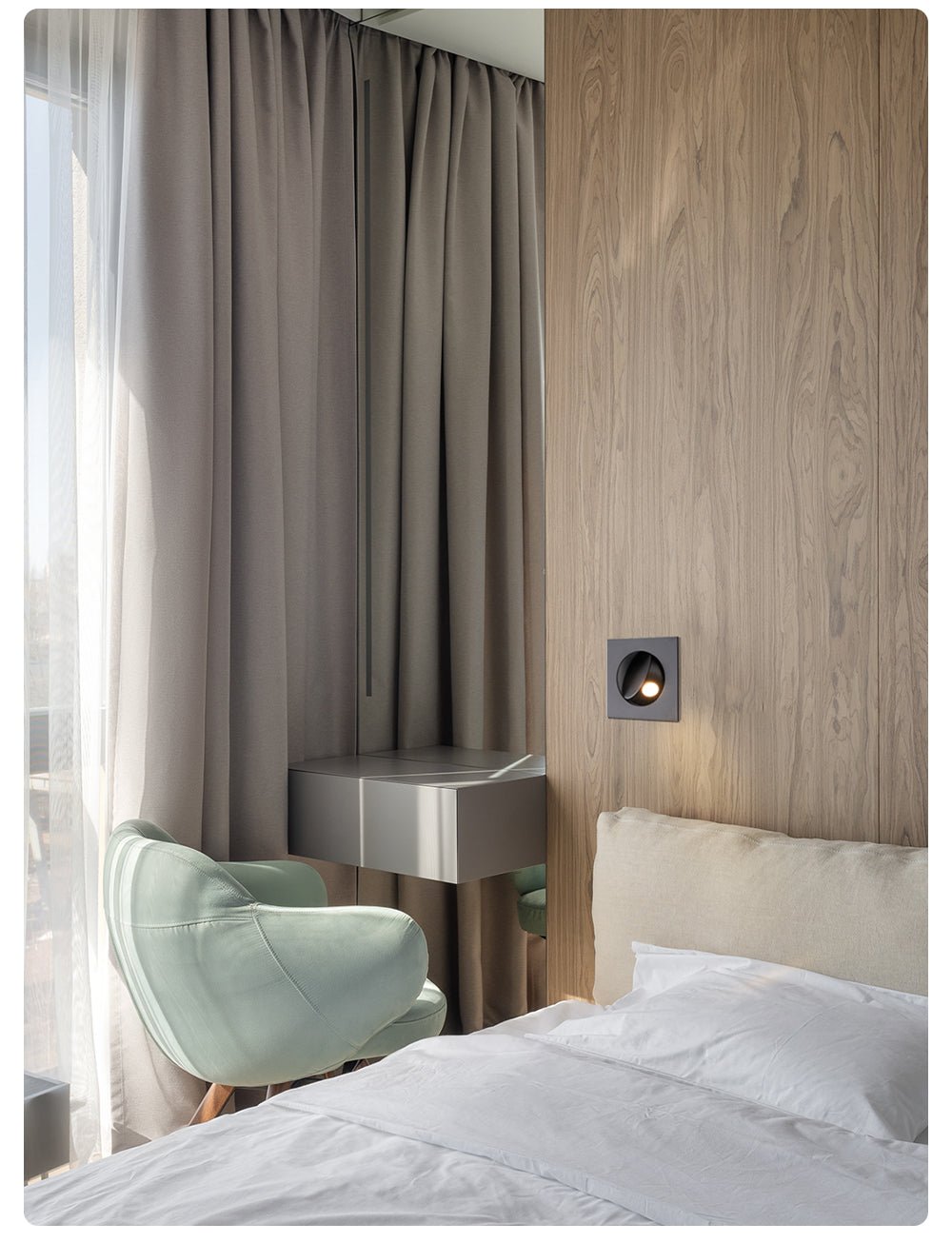 Wide view of a black Clérachic recessed wall light in a wood-panelled wall, next to full-length curtains and a made bed.