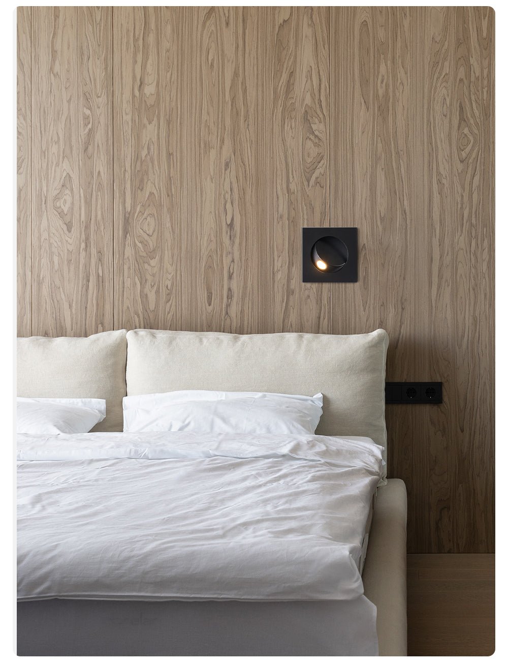 Black Clérachic recessed wall light set into a wood-grain wall above the headboard of a bed with white bedding.