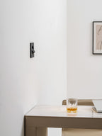 Side-on view of this Clérachic recessed wall light with its hood turned, on a white wall above a marble desk and a glass.