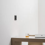 The black Clérachic recessed wall light seen from the side on a white wall, with a glass and a laptop on the desk below.