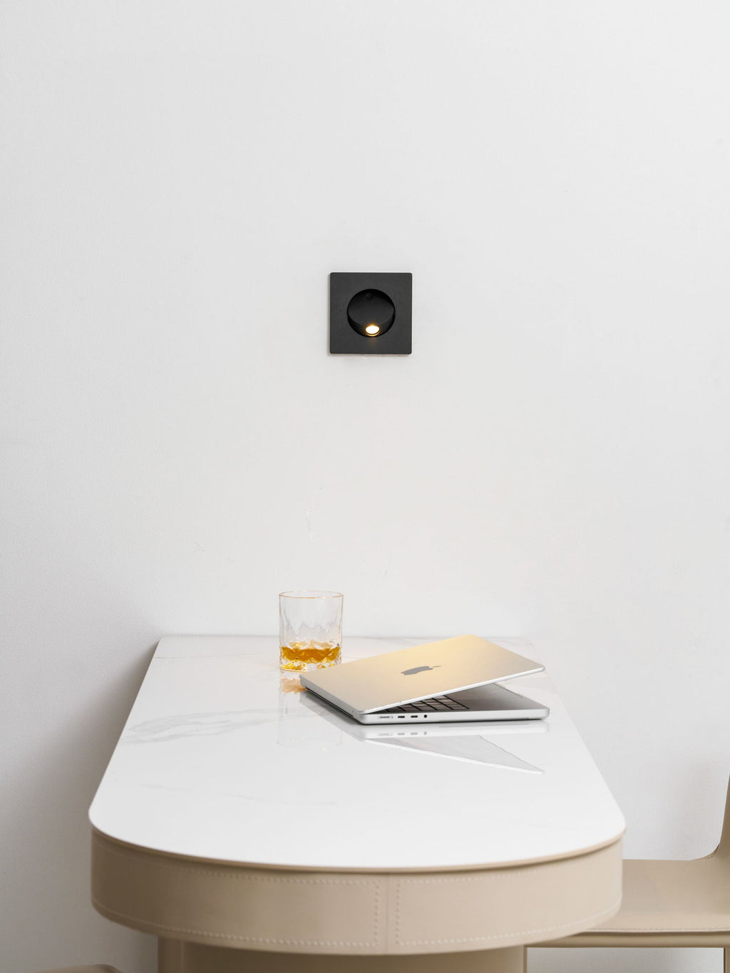 Black Clérachic recessed wall light above a curved cream desk top, with a glass of whisky and a laptop beneath.