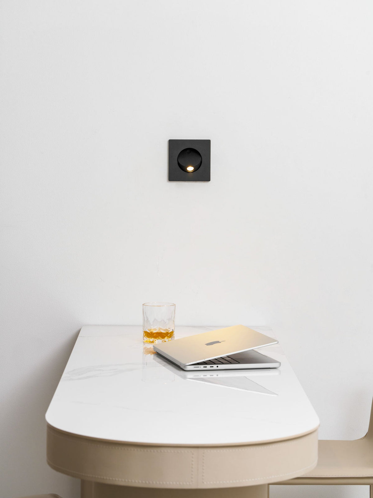 Black Clérachic recessed wall light above a curved cream desk top, with a glass of whisky and a laptop beneath.