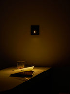 This Clérachic recessed wall light lights a desk with a whisky glass and a notebook, with the rest of the room in shadow.