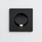 Front close view of the square black Clérachic recessed wall light, with its round opening, hood and warm LED lit.
