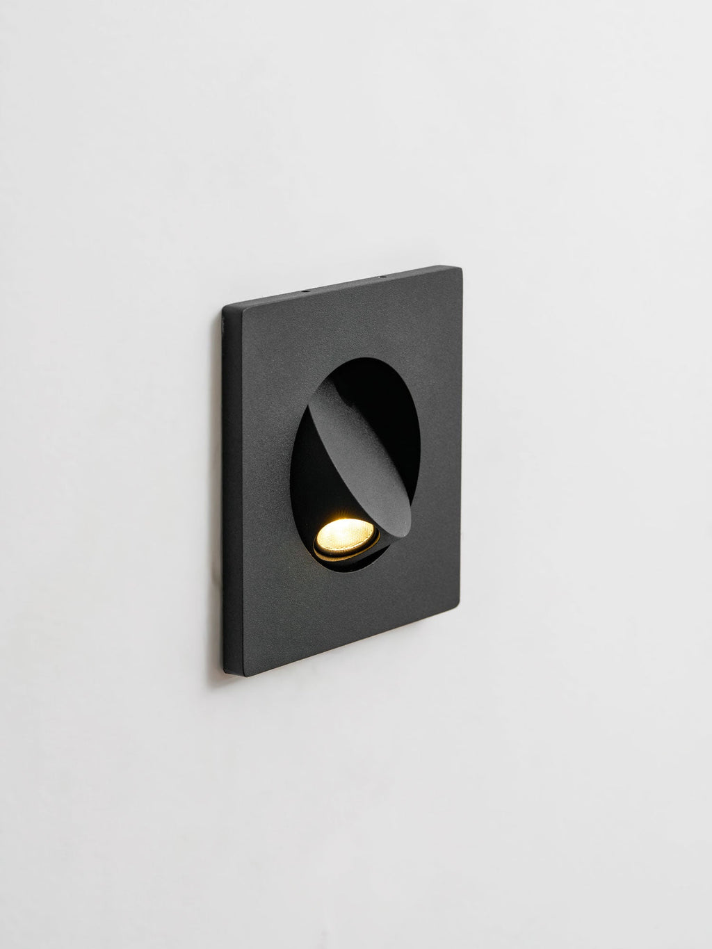 Angled view of this black Clérachic recessed wall light, with the hood tilted to one side and the LED lit.
