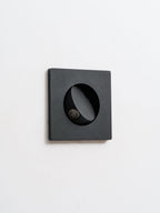 Unlit black Clérachic recessed wall light seen at a slight angle, with the hood turned to one side over the LED.