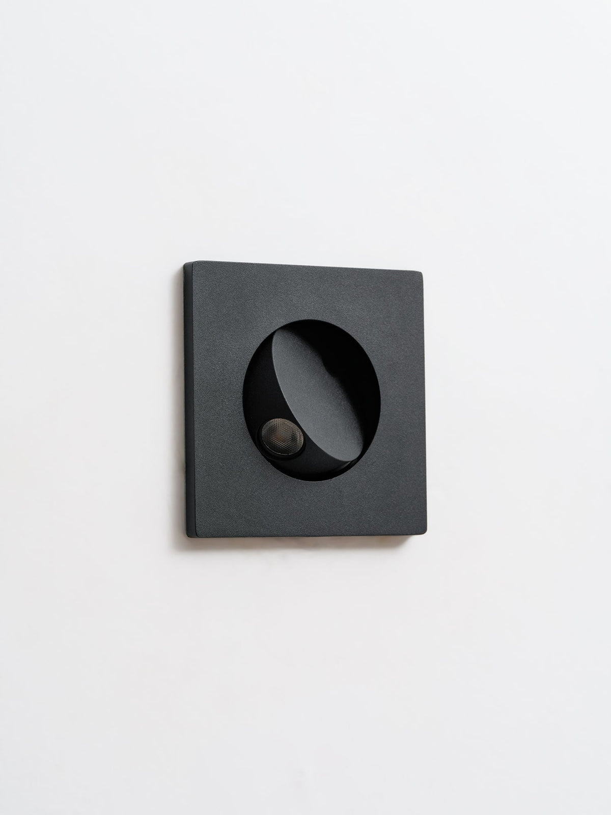 Unlit black Clérachic recessed wall light seen at a slight angle, with the hood turned to one side over the LED.