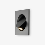 Close angled view of the black Clérachic recessed wall light, with the hood swung out and the lit LED aimed downward.