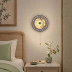A Clérachic wall light with a bamboo-pattern porcelain shade above a bedside table, beside a sage-green pillow and a small vase of blossom.
