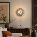 Lit Clérachic porcelain wall light glowing softly above a dark wood sideboard, with a rust cushion on a cream sofa below.