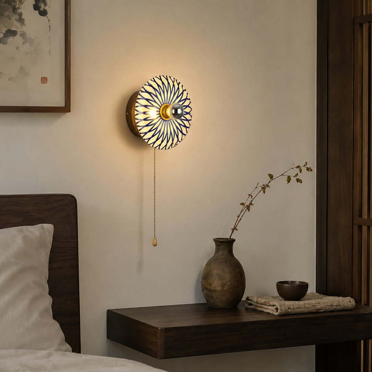 Lit Clérachic wall light with a blue and white petal-pattern shade on a wood backplate, above a floating shelf with a stoneware vase.