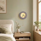 Blue and white Clérachic wall light on a sage-green wall, above a pale bedside table with a vase of blossom and a stack of books.