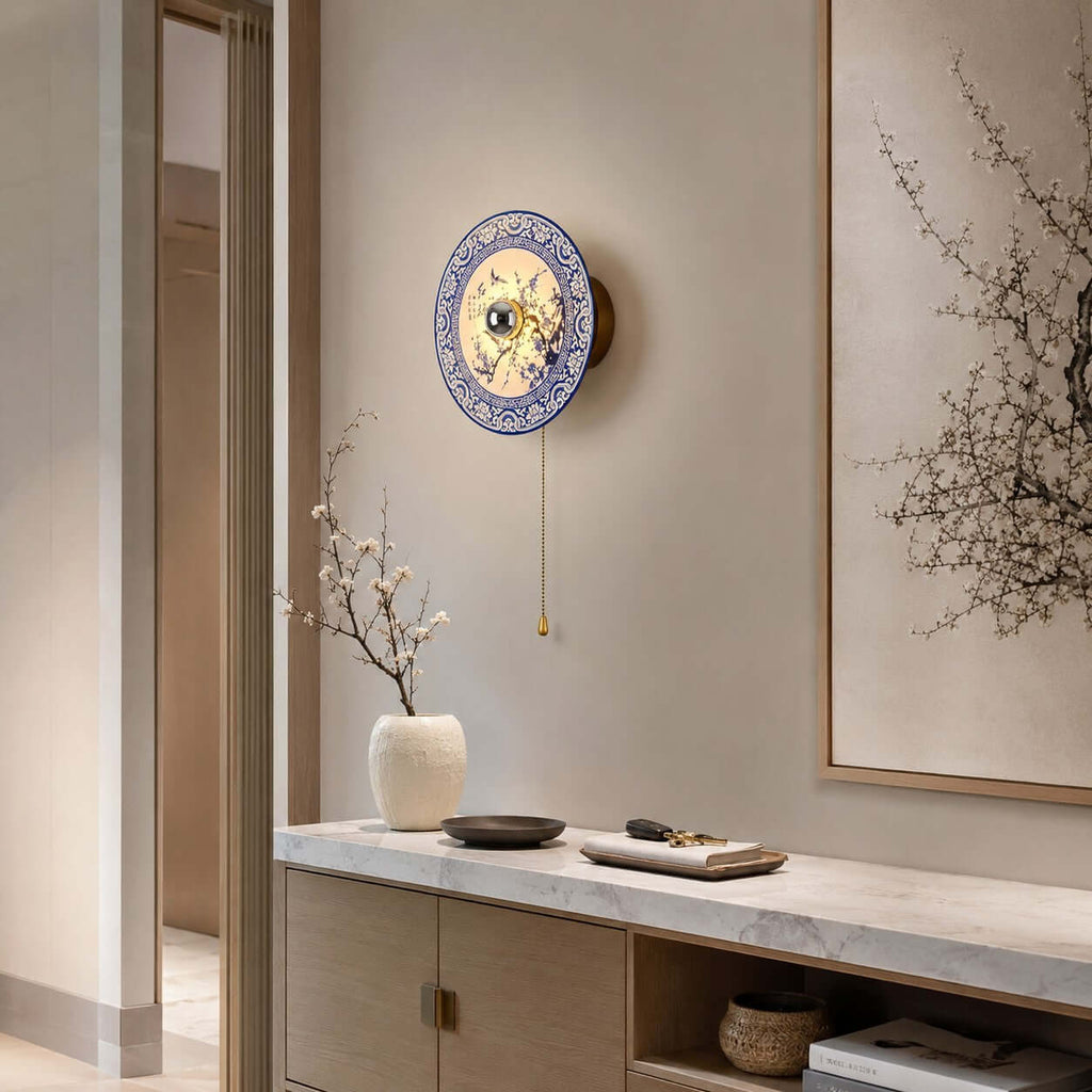 Clérachic porcelain wall light on a plain wall above a marble-topped cabinet, with a framed branch print and a white vase of blossom.
