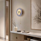 Clérachic porcelain wall light on a plain wall above a marble-topped cabinet, with a framed branch print and a white vase of blossom.