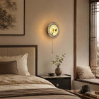 Lit Clérachic wall light with a dark wood backplate, above a made bed with linen pillows and a window seat to the right.