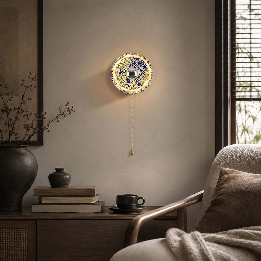 Clérachic wall light with a swirl-pattern blue and white shade, lit above a stack of books and a coffee cup beside a lounge chair.