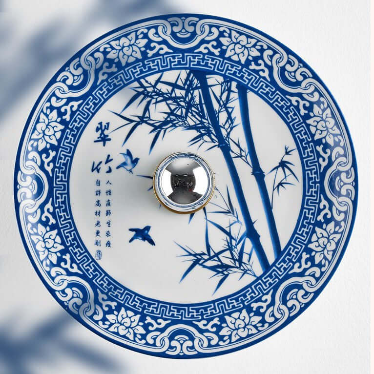 Close view of the blue bamboo and bird design on this Clérachic wall light's porcelain shade, with its mirrored centre boss.