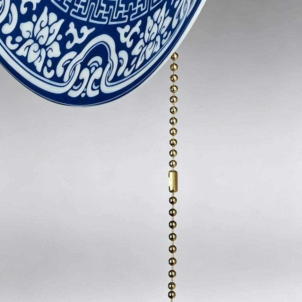 Close view of the brass bead pull chain and the scrolling blue border on the edge of this Clérachic wall light.