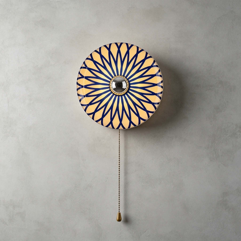 Round Clérachic wall light with a blue and white petal pattern radiating from its mirrored centre, a brass chain below.