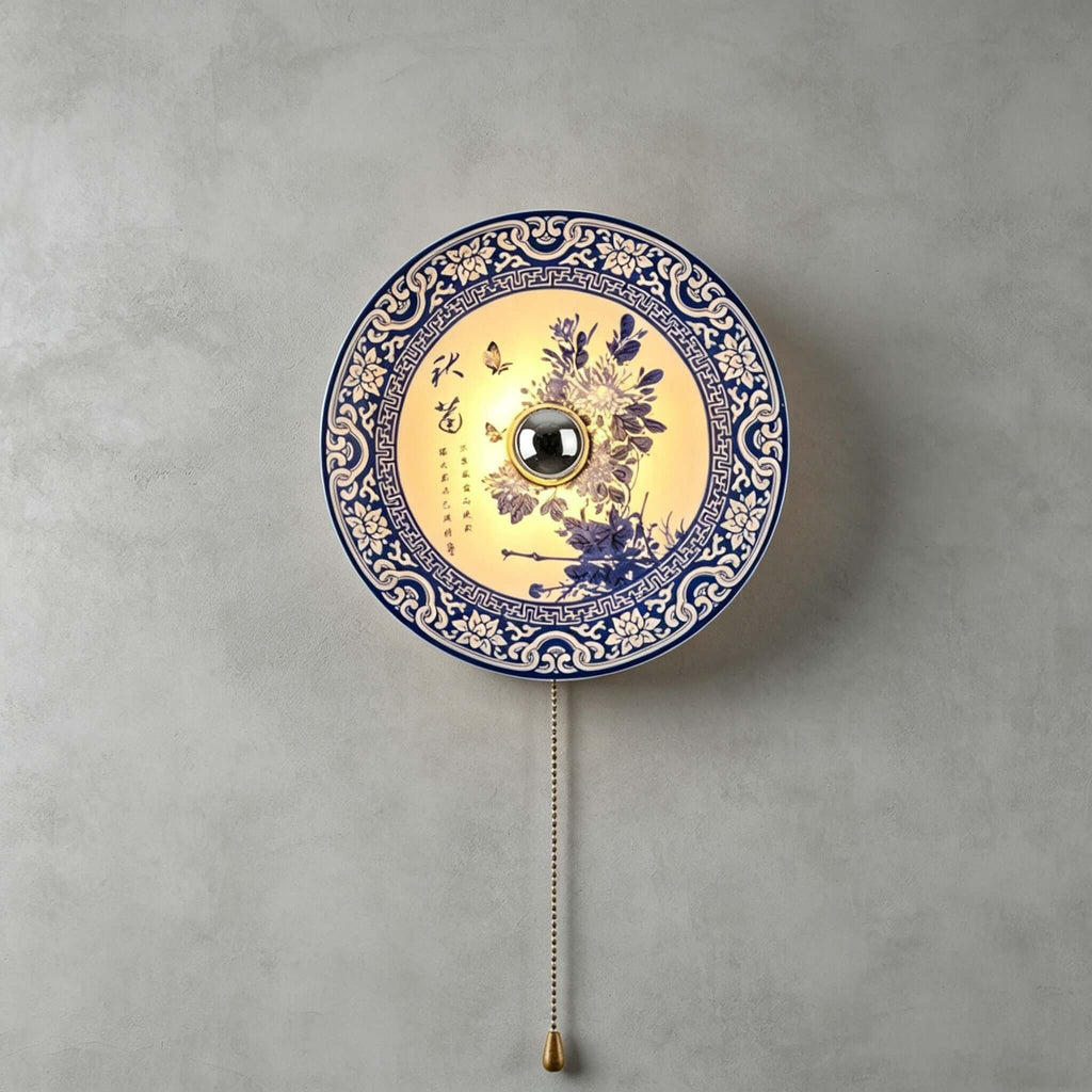 Clérachic wall light with a purple-blue chrysanthemum design inside a blue lattice border, lit, on a grey concrete wall.
