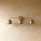 Clérachic three-light bar sconce in polished brass, shown from a slightly closer studio angle on a plaster wall.