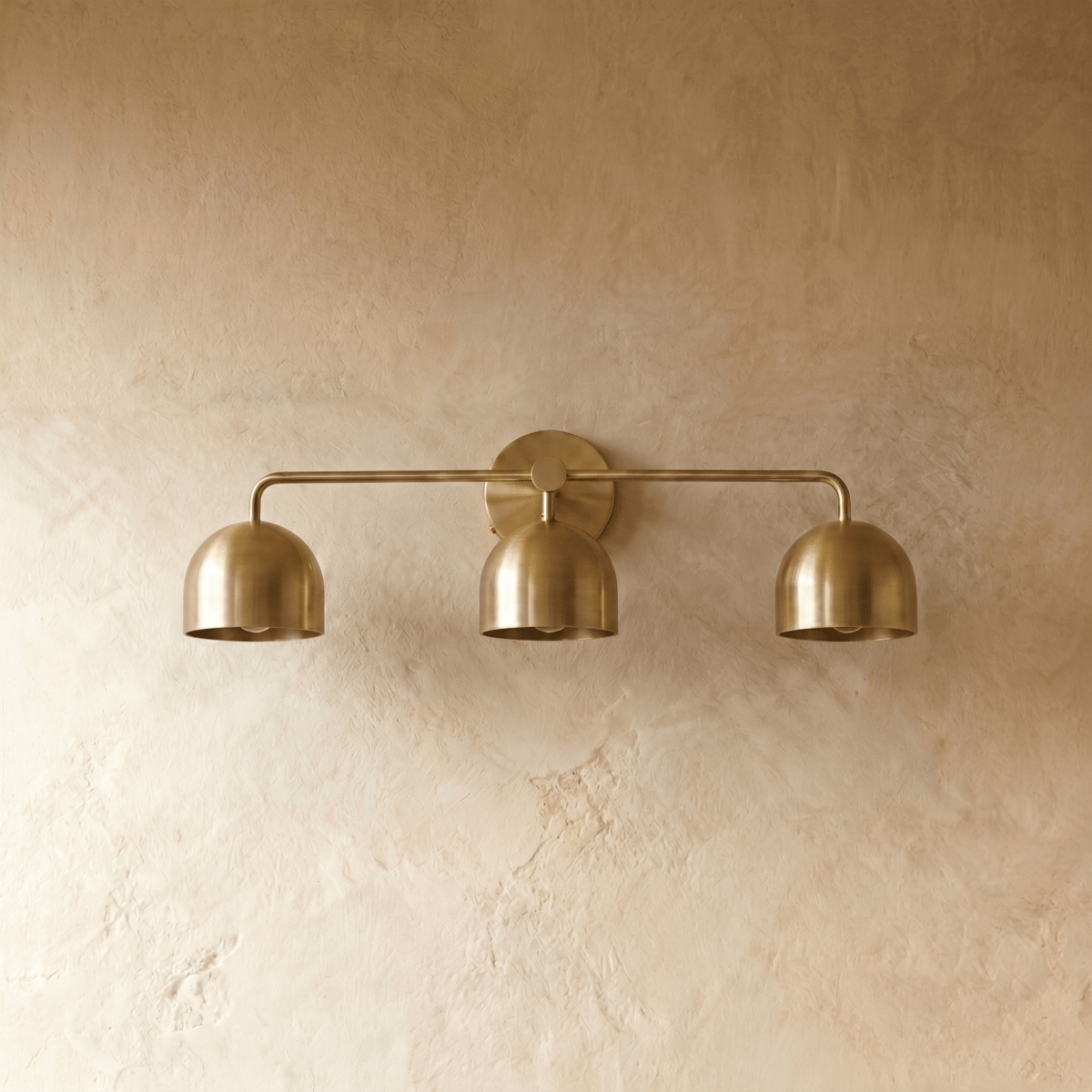 Clérachic three-light bar sconce in polished brass, shown from a slightly closer studio angle on a plaster wall.