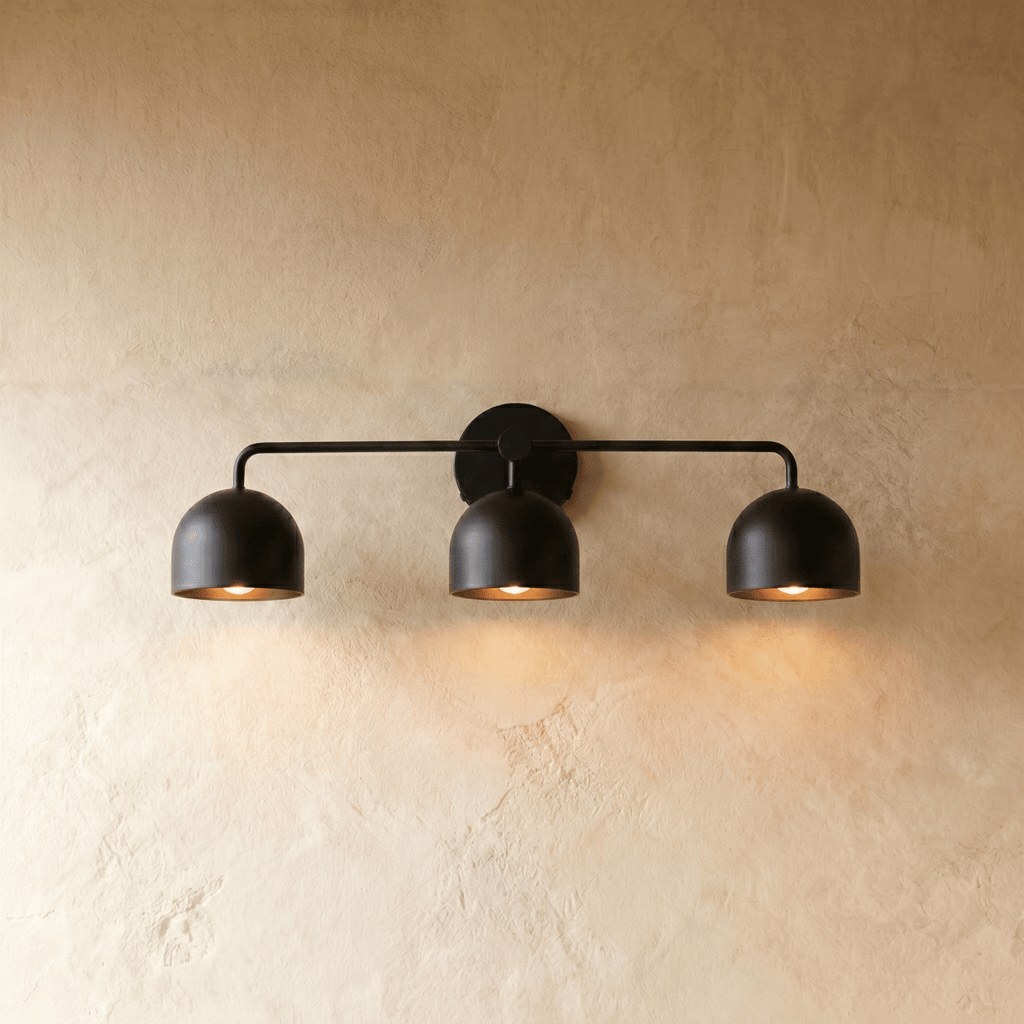 Clérachic three-light bar sconce in matte black with dome shades, mounted on a plaster wall in studio light.