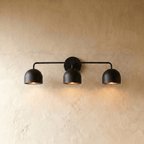 Clérachic three-light bar sconce in matte black with dome shades, mounted on a plaster wall in studio light.