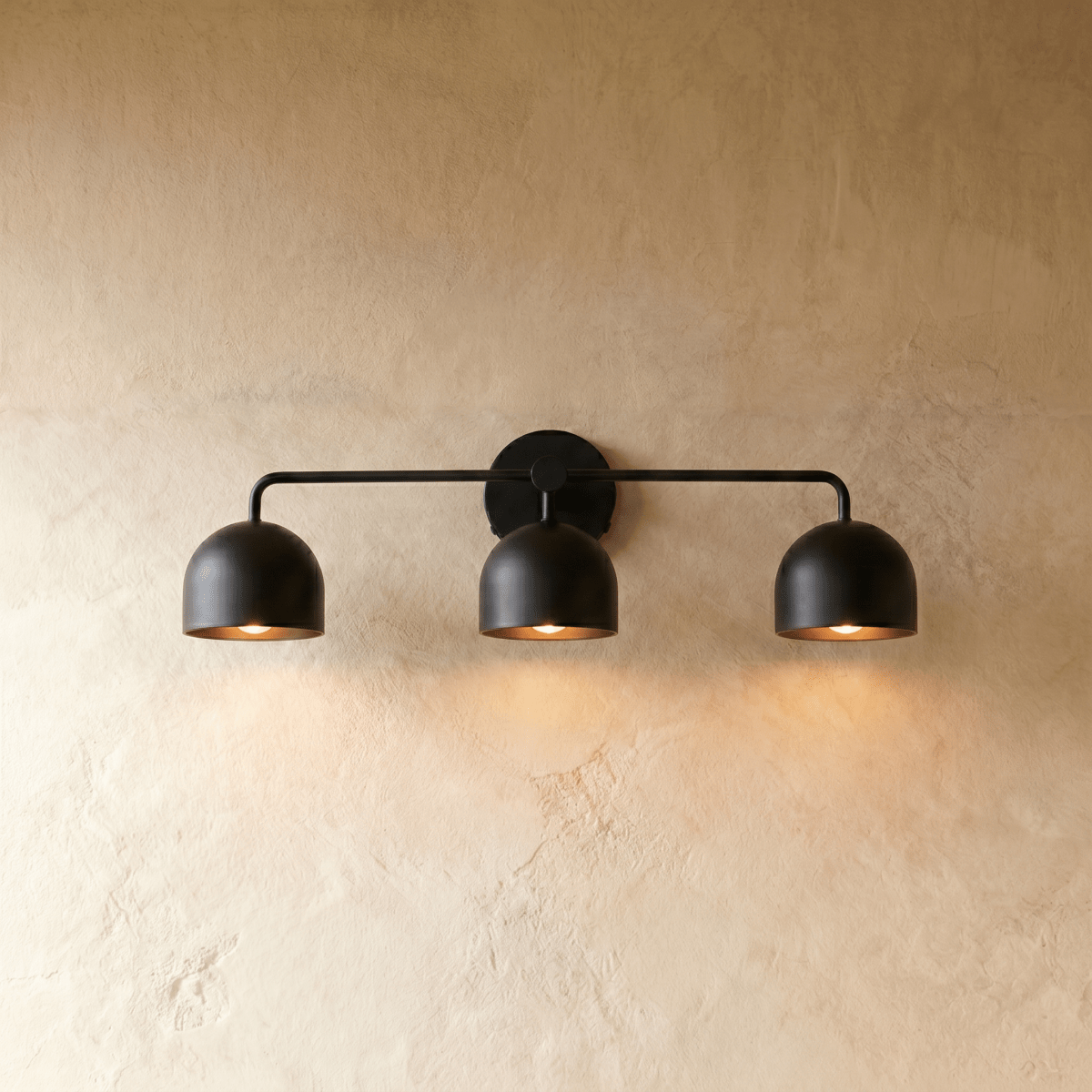 Clérachic three-light bar sconce in matte black with dome shades, mounted on a plaster wall in studio light.