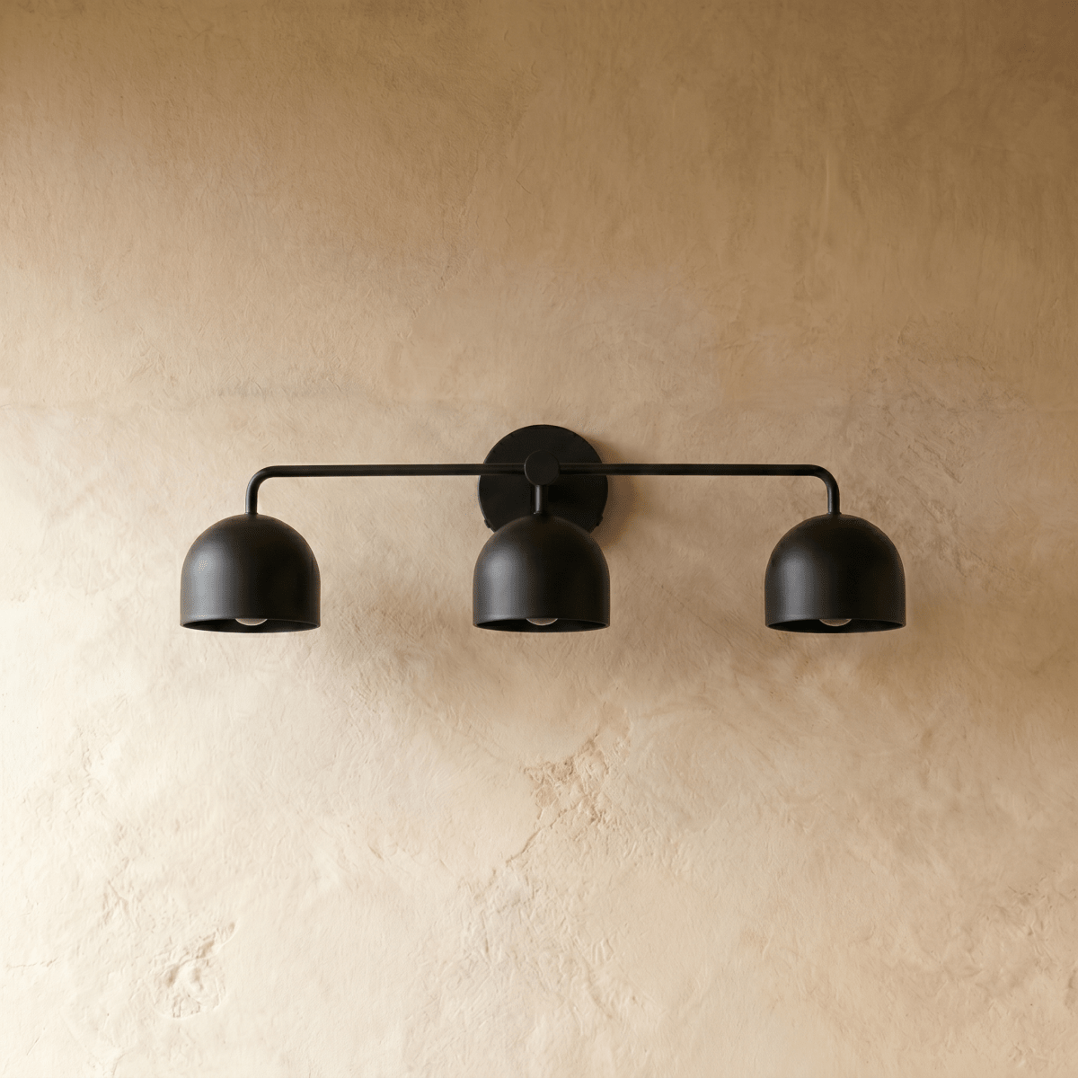 Clérachic three-light bar sconce in matte black, shown from a slightly closer studio angle on a plaster wall.