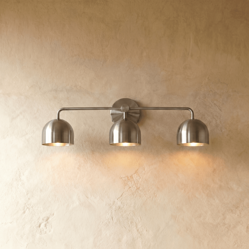 Clérachic three-light bar sconce in chrome with dome shades, mounted on a plaster wall in studio light.