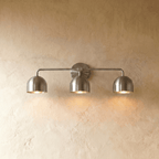 Clérachic three-light bar sconce in chrome with dome shades, mounted on a plaster wall in studio light.
