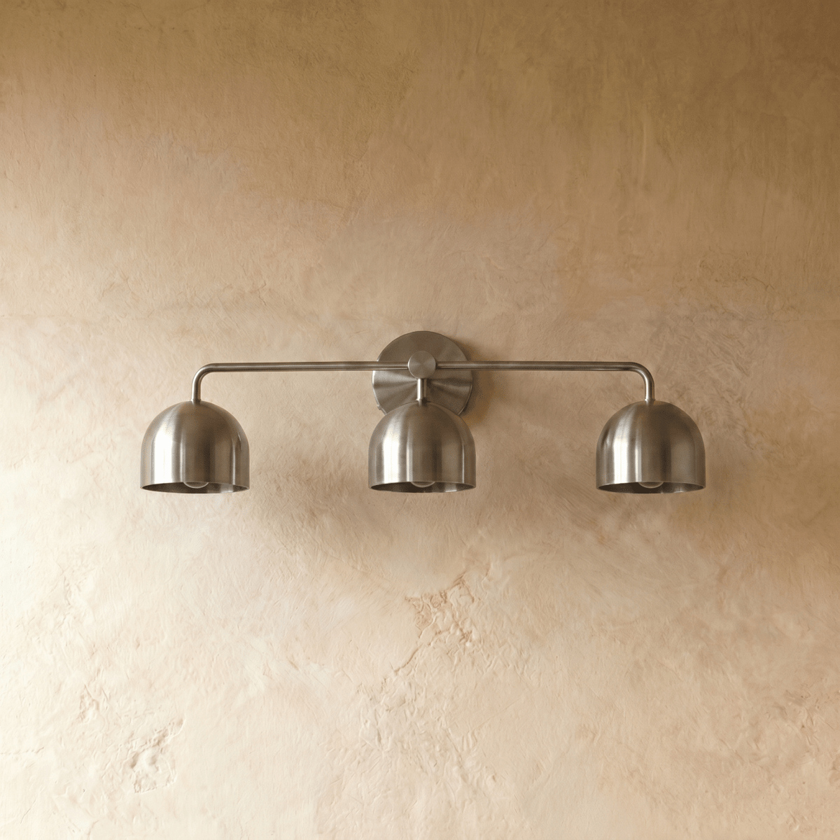 Clérachic three-light bar sconce in chrome, shown from a slightly closer studio angle on a plaster wall.
