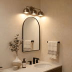 Clérachic vintage brass three-light bar sconce lit above an arched mirror over a bathroom vanity sink.