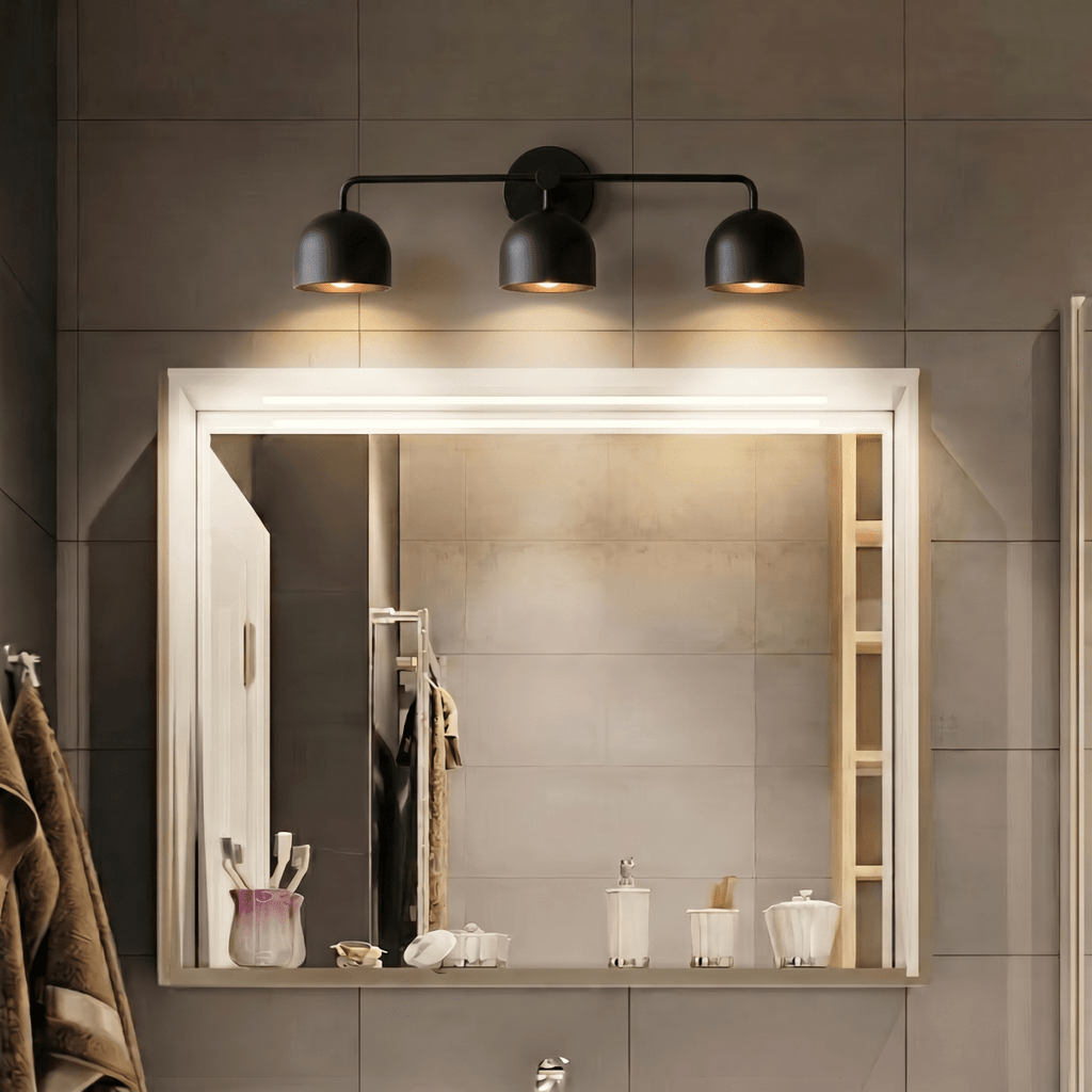 Clérachic matte black three-light bar sconce lit above a large backlit mirror in a tiled bathroom.