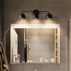 Clérachic matte black three-light bar sconce lit above a large backlit mirror in a tiled bathroom.