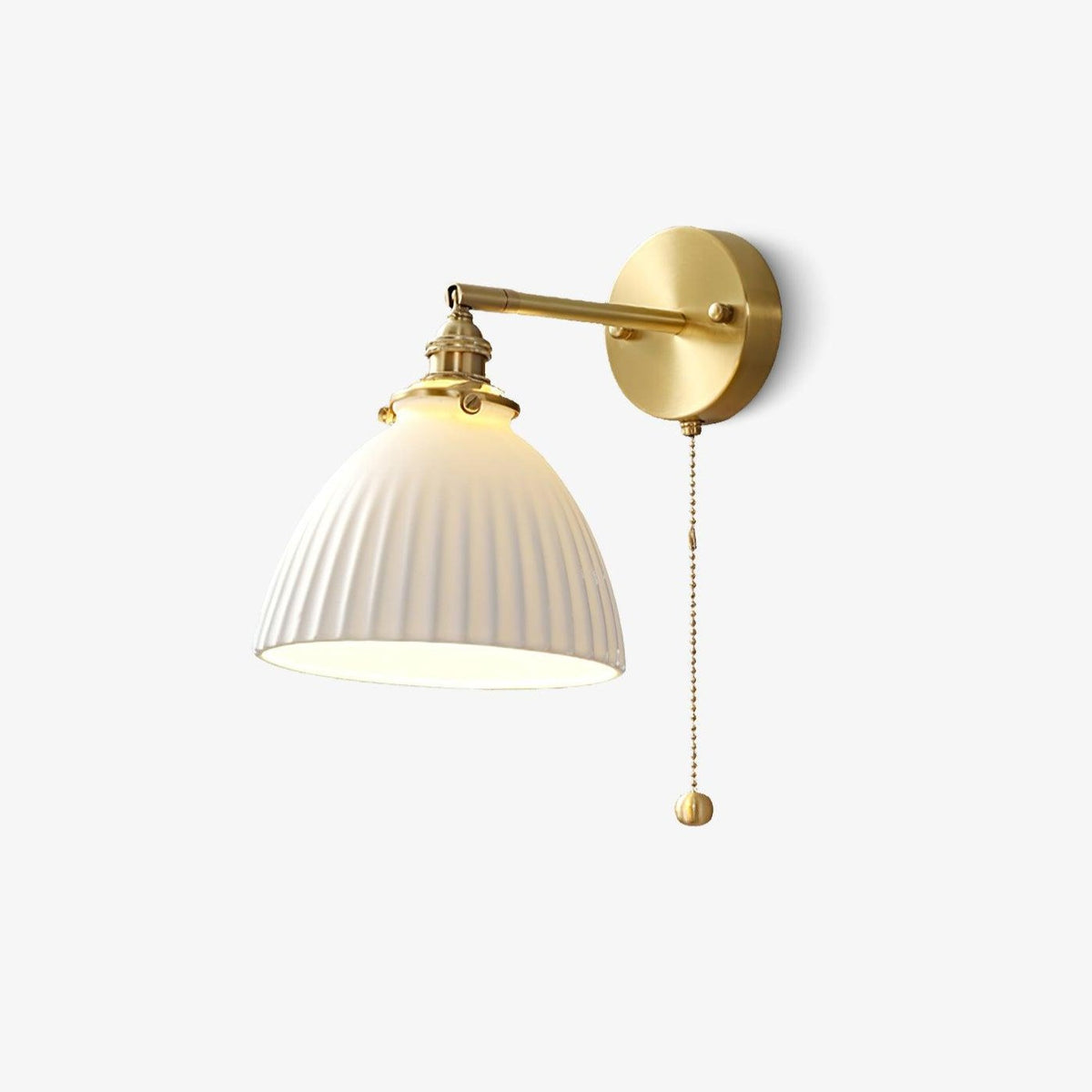 Brass wall light from Clérachic with a pleated white ceramic shade and a beaded pull chain, on a plain white backdrop.